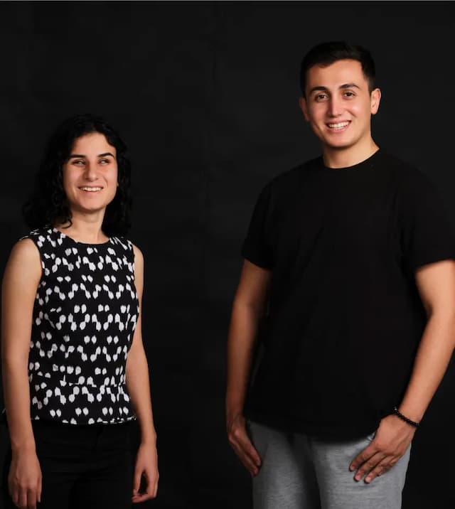 Sadriye and Cihat are posing happily for the camera on a black background. Sadriye is wearing a t-shirt with black and white horizontal stripes, while Cihat is wearing a black t-shirt.