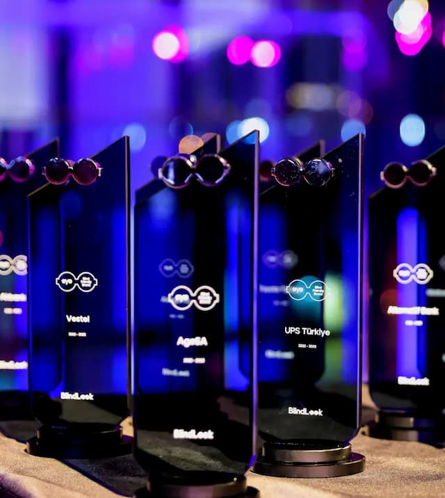 On a table under dim lighting, there are glass and transparent awards that will be presented at the EyeBrand Ceremony.